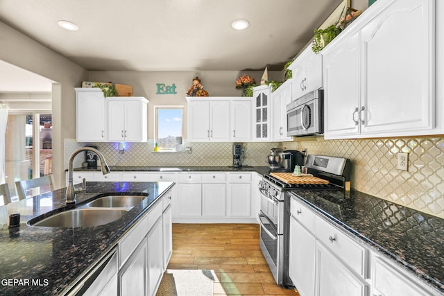 kitchen featuring white cabinetry, sink, stainless steel appliances, dark stone countertops, and light hardwood / wood-style floors