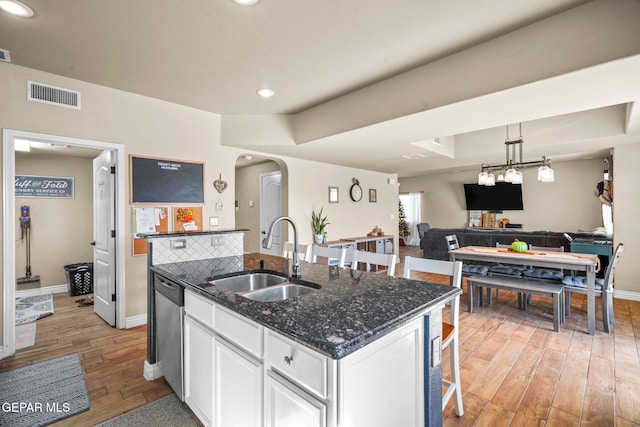 kitchen featuring white cabinetry, sink, dark stone counters, a kitchen bar, and a center island with sink