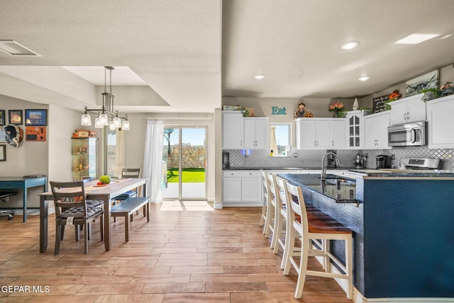 kitchen with tasteful backsplash, a breakfast bar, a textured ceiling, decorative light fixtures, and white cabinetry