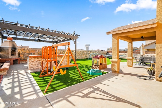 view of playground featuring an outdoor stone fireplace, a pergola, and a patio