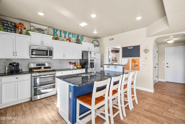 kitchen featuring a kitchen bar, stainless steel appliances, sink, a center island with sink, and white cabinetry