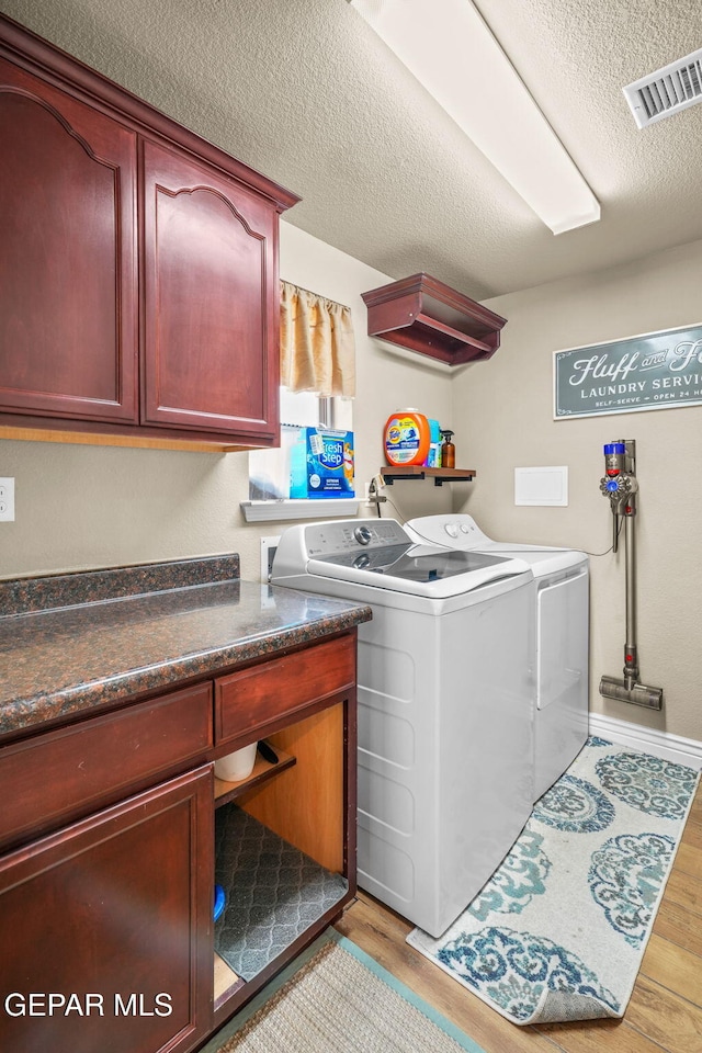 laundry area with washer and clothes dryer, cabinets, a textured ceiling, and light wood-type flooring