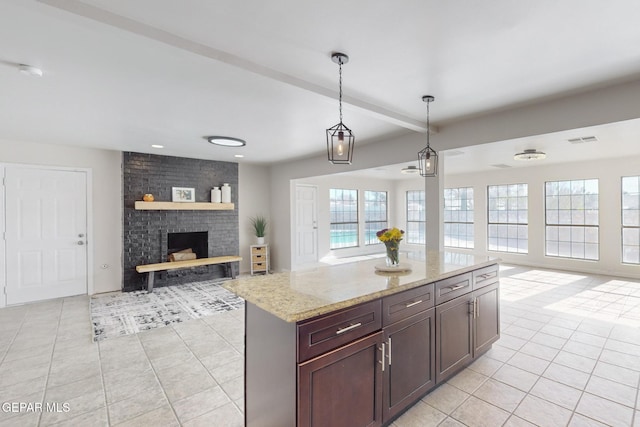 kitchen with pendant lighting, a center island, a brick fireplace, light tile patterned floors, and light stone counters