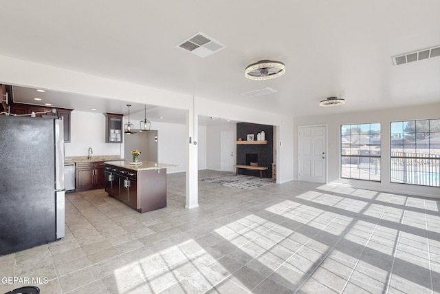 kitchen featuring dark brown cabinetry, a center island, dishwasher, stainless steel fridge, and pendant lighting