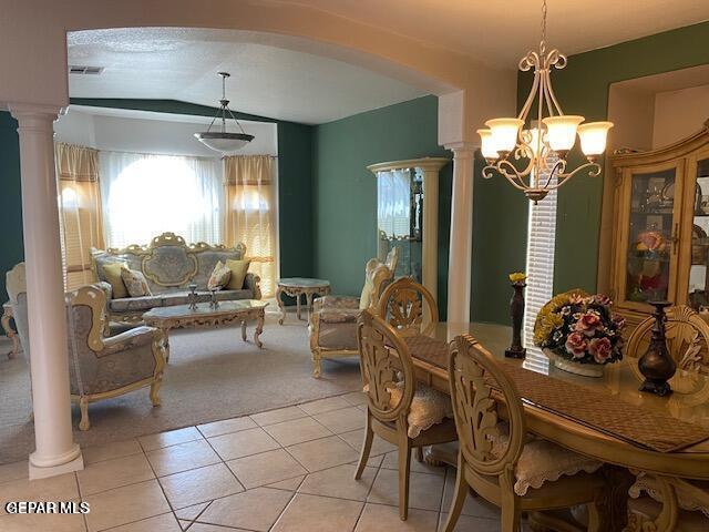 dining room with decorative columns, light tile patterned floors, vaulted ceiling, and an inviting chandelier