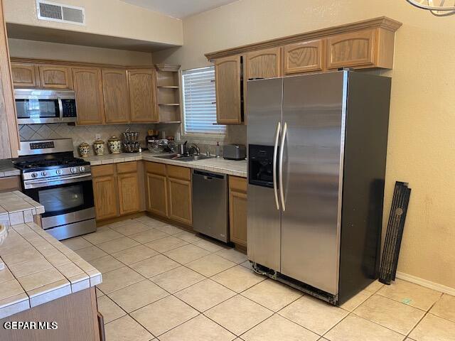 kitchen with backsplash, stainless steel appliances, sink, light tile patterned floors, and tile counters