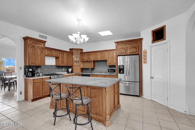 kitchen featuring light tile patterned flooring, decorative light fixtures, appliances with stainless steel finishes, a notable chandelier, and a kitchen island