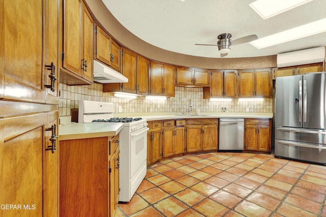 kitchen with appliances with stainless steel finishes, backsplash, ceiling fan, a wall mounted AC, and sink