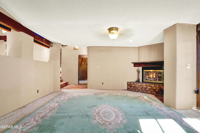 living room with ceiling fan, beamed ceiling, a textured ceiling, and a brick fireplace