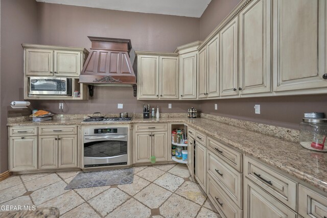 kitchen featuring light stone countertops, premium range hood, stainless steel appliances, and cream cabinets