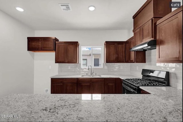 kitchen featuring backsplash, light stone counters, black gas stove, and sink