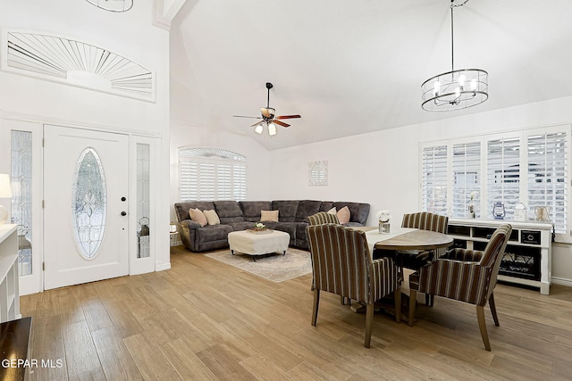 dining room featuring a healthy amount of sunlight, high vaulted ceiling, wood-type flooring, and ceiling fan with notable chandelier