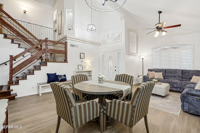 dining space featuring light wood-type flooring, a towering ceiling, and ceiling fan with notable chandelier