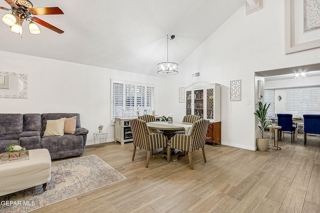 dining space featuring ceiling fan with notable chandelier and high vaulted ceiling