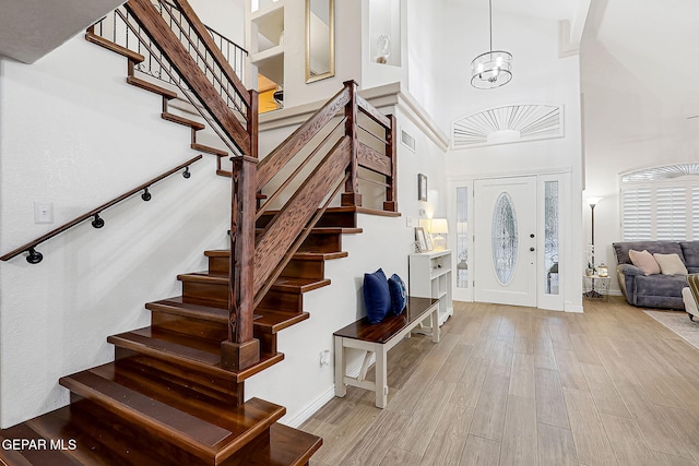 foyer entrance featuring light hardwood / wood-style flooring, a towering ceiling, and a notable chandelier