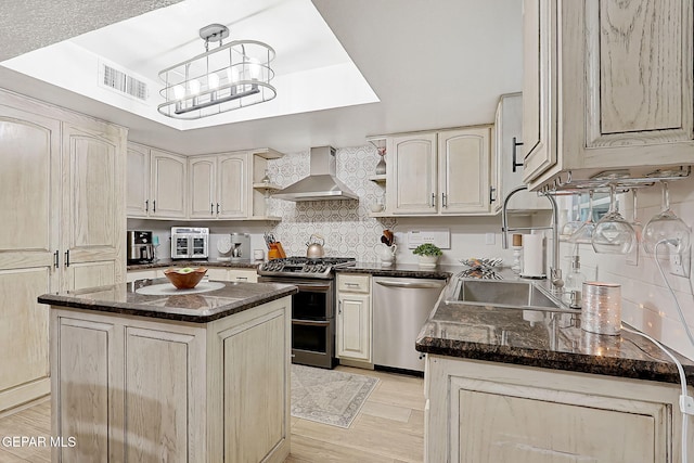 kitchen featuring appliances with stainless steel finishes, sink, wall chimney range hood, a center island, and hanging light fixtures