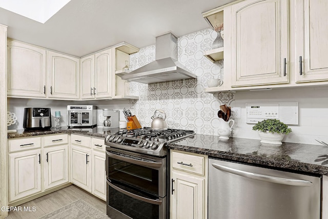 kitchen featuring decorative backsplash, light wood-type flooring, wall chimney exhaust hood, stainless steel appliances, and dark stone countertops