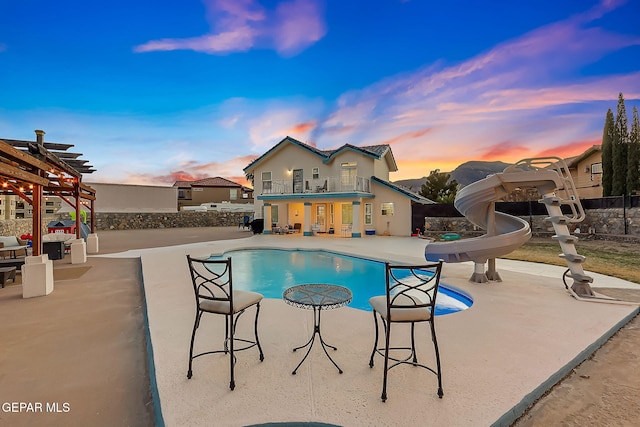 pool at dusk featuring a pergola, a patio area, and a water slide