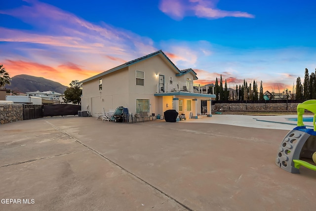 back house at dusk with a mountain view, a patio, and a balcony