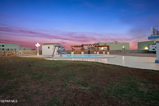 pool at dusk with a patio area, a lawn, a storage shed, and a water slide