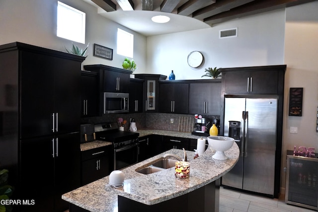 kitchen featuring light stone countertops, stainless steel appliances, sink, wine cooler, and an island with sink