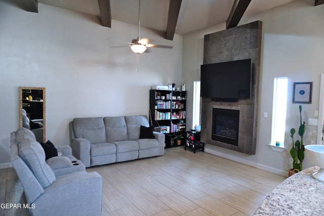 living room featuring beamed ceiling, ceiling fan, and a tiled fireplace