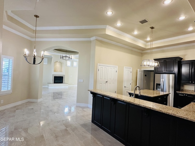 kitchen with a raised ceiling, light stone counters, pendant lighting, and stainless steel refrigerator with ice dispenser