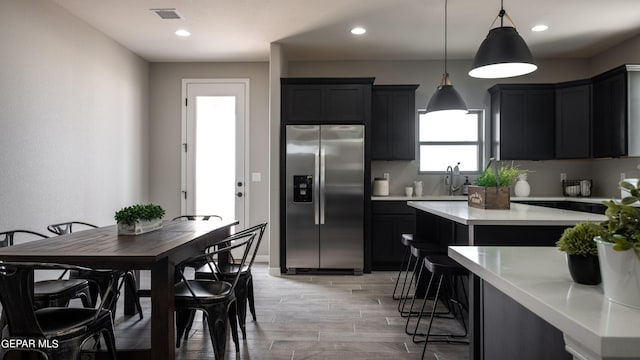 kitchen featuring pendant lighting, a breakfast bar, a center island, sink, and stainless steel fridge with ice dispenser