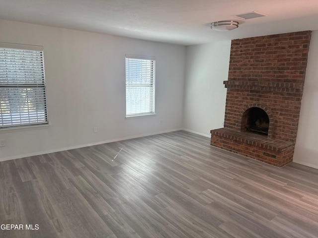 unfurnished living room featuring a brick fireplace, visible vents, baseboards, and wood finished floors