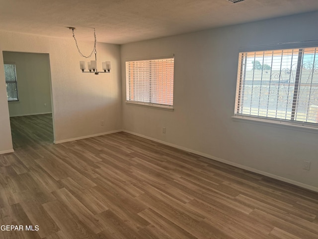 spare room featuring dark wood-type flooring, a notable chandelier, and baseboards