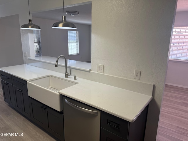 kitchen with dark cabinets, hanging light fixtures, light countertops, stainless steel dishwasher, and a sink