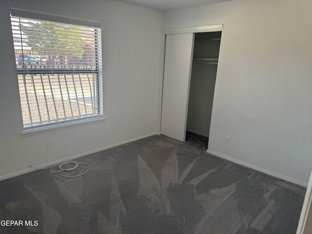 unfurnished bedroom featuring dark colored carpet, a closet, and baseboards