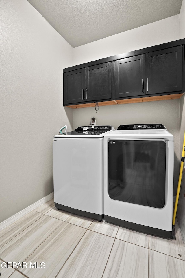 clothes washing area featuring washing machine and dryer, cabinets, and a textured ceiling