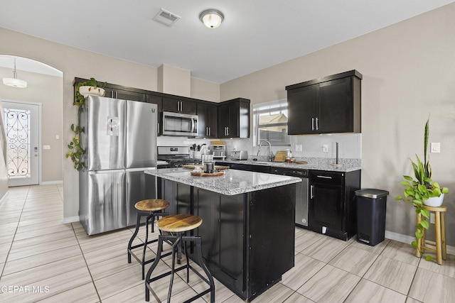 kitchen featuring appliances with stainless steel finishes, light stone counters, light tile patterned floors, a kitchen island, and a breakfast bar area