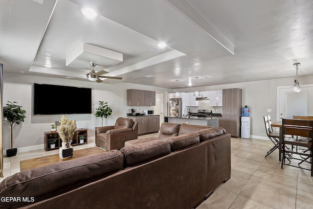 tiled living room featuring a tray ceiling, ceiling fan, and sink