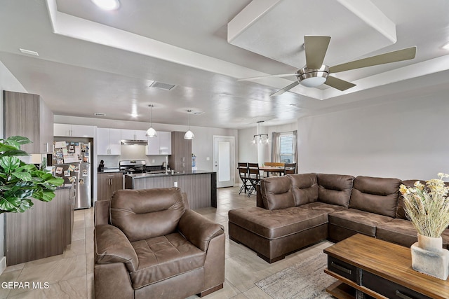 living room featuring ceiling fan with notable chandelier, a raised ceiling, and sink