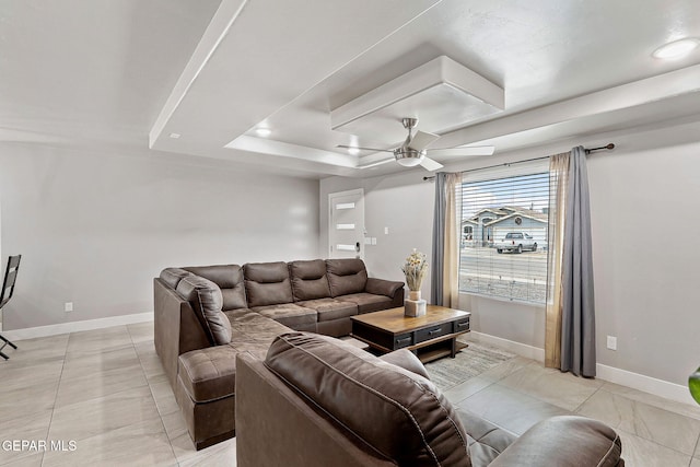 living room with a tray ceiling, ceiling fan, and light tile patterned flooring