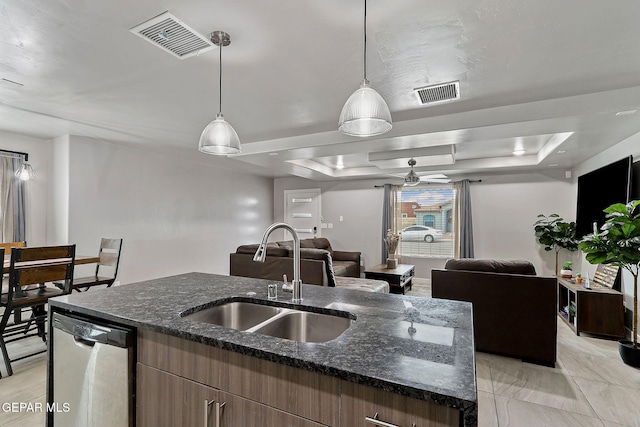 kitchen with pendant lighting, a raised ceiling, sink, stainless steel dishwasher, and an island with sink