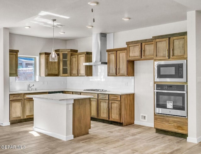 kitchen featuring light wood-type flooring, wall chimney exhaust hood, stainless steel appliances, pendant lighting, and a kitchen island