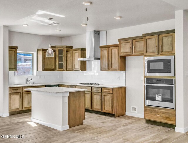 kitchen with light hardwood / wood-style flooring, wall chimney exhaust hood, decorative light fixtures, a kitchen island, and stainless steel appliances