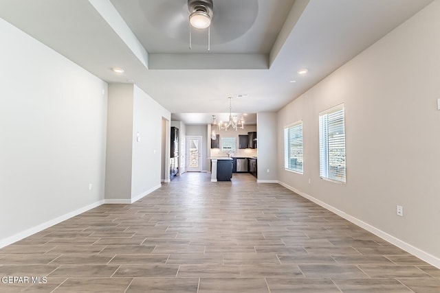 unfurnished living room with a raised ceiling and ceiling fan with notable chandelier