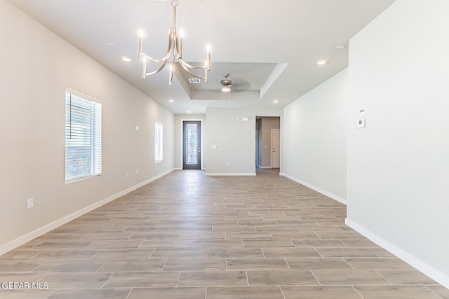 spare room featuring plenty of natural light, a raised ceiling, and ceiling fan with notable chandelier