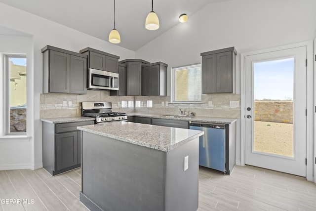 kitchen with hanging light fixtures, lofted ceiling, gray cabinets, a kitchen island, and appliances with stainless steel finishes