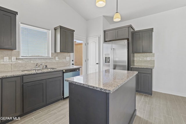 kitchen with gray cabinetry, stainless steel appliances, sink, pendant lighting, and a kitchen island