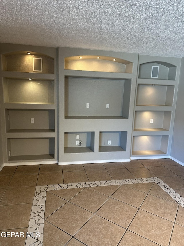 unfurnished living room featuring built in shelves, a textured ceiling, and dark tile patterned floors