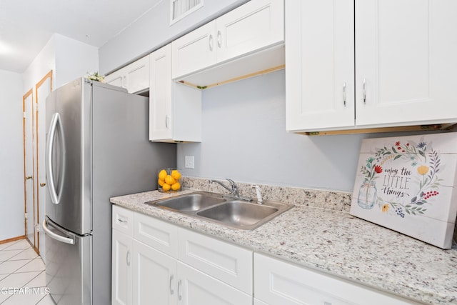 kitchen with white cabinets, light tile patterned flooring, light stone countertops, and sink