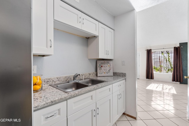 kitchen featuring white cabinets, light tile patterned floors, light stone counters, and sink