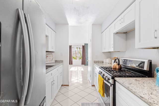 kitchen with appliances with stainless steel finishes, light stone counters, a textured ceiling, light tile patterned floors, and white cabinetry