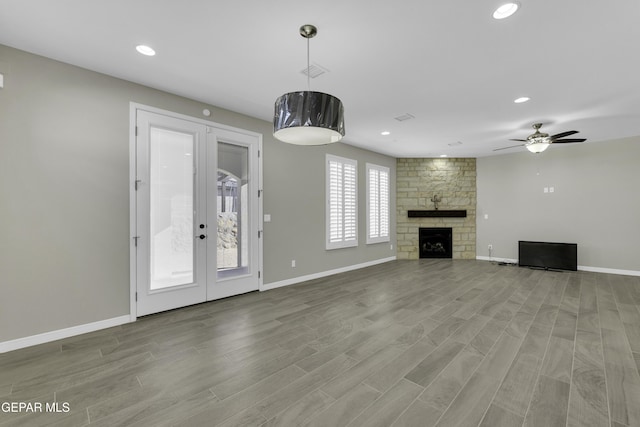 unfurnished living room featuring ceiling fan, light hardwood / wood-style floors, a stone fireplace, and french doors