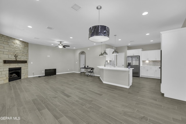 kitchen with white cabinets, a stone fireplace, hanging light fixtures, ceiling fan, and stainless steel fridge